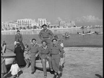 ...mentre in un�altra immagine rappresenta un gruppo di sorridenti commilitoni in posa su un gozzo, tipico natante dei pescatori baresi

(F. Alexander Turnbull Library, Welligton, NZ. Ref. DA-04513-F)